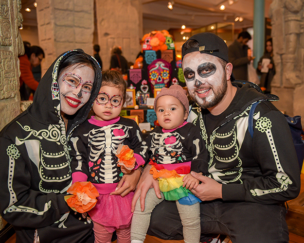 family in skull makeup and skeleton outfits smiling in gallery.