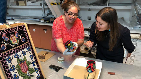 staffer and faculty look at beaded items in conservation lab.