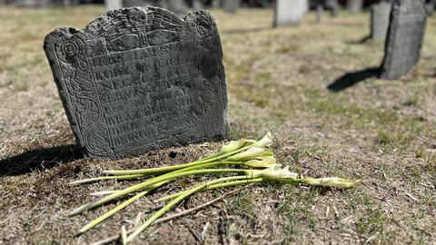 An old headstone in a graveyard with fresh flowers laid before it.