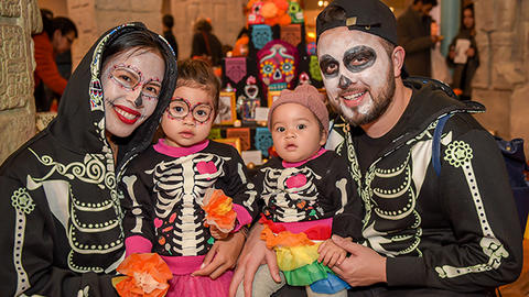 family in skull makeup and skeleton outfits smiling in gallery.