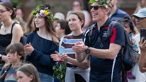 audience wearing flower crowns outside museum applaud.