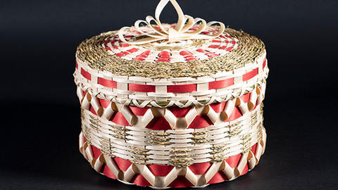 Small red and white hand woven basket against a black background