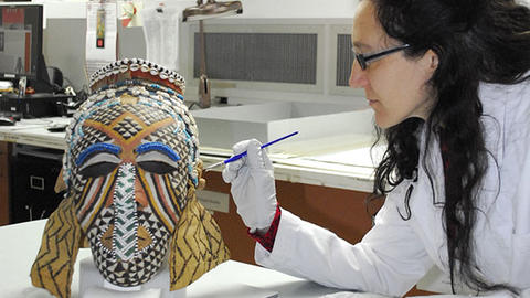 conservator works with kuba mask in lab.