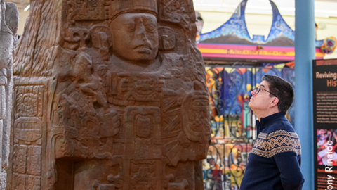 man faces large maya sculptures in colorful gallery.