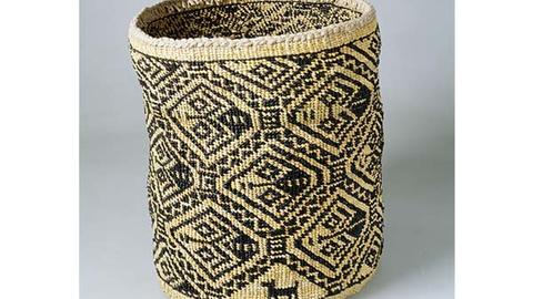 Cylindrical woven fiber basket in light and dark contrasting fibers.