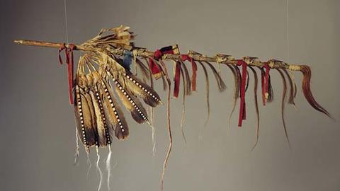 Ceremonial pipe decorated with striped feathers and red and blue ribbon.