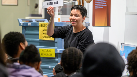 educator holds up artifact sign in gallery with elementary school students.