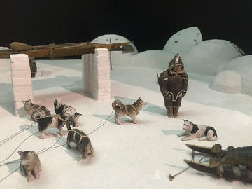 arctic diorama with person in fur coat, kayak, sled, and sled dogs