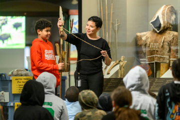 igloos class watches museum educator stand with a student holding a harpoon.