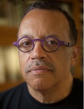 Portrait of Wendel White. He looks directly into the lens wearing purple circular glasses.