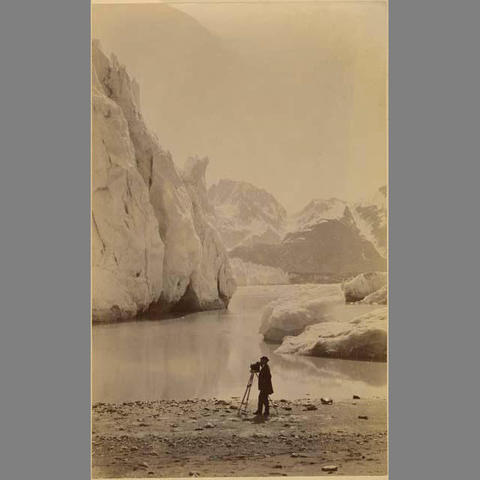 man with an antique camera standing next a lake.