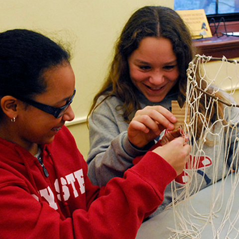 two smiling girls examine net in foragers to farmers classroom.