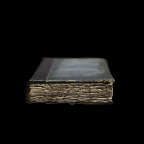 an old book with rough pages in focus and the blurry cover facing up and away from view.