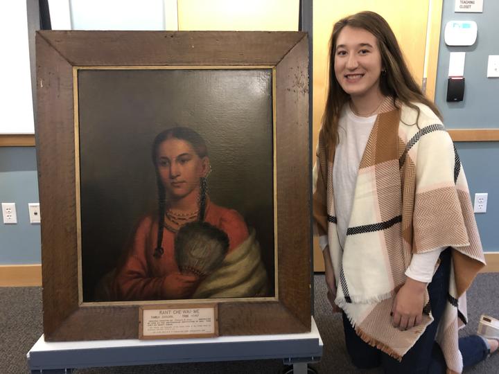 Young woman standing next to a painted portrait