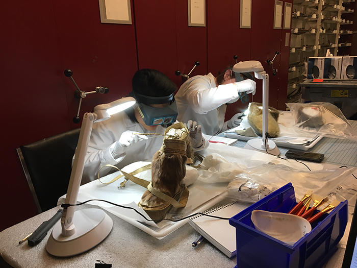 Two people in lab coats sitting at a table cleaning objects
