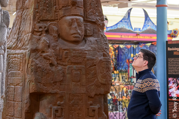 man faces large maya sculptures in colorful gallery.