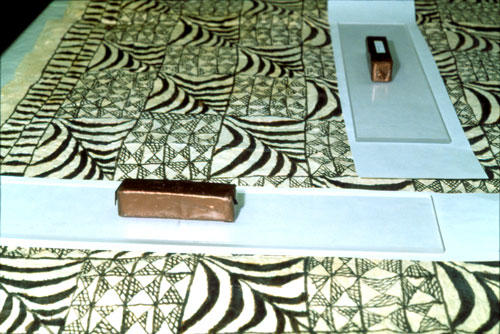 brick-shaped weights on top of glass strip on top of blotter paper strip on top of tapa.