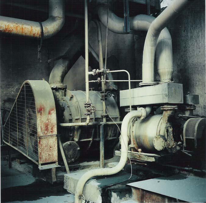 Greenish pipes route in and out of the frame, centralized to a machine with a large fan in the center.
