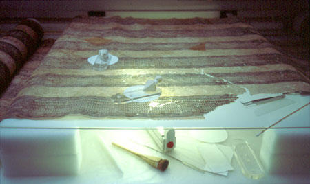 decorated tapa spread out on glass with lighting below that revealstears.