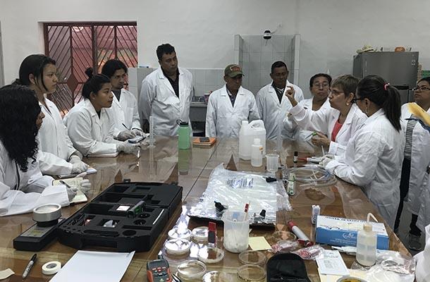 Group in white lab coats around a table in Conservation lab listening to instructor