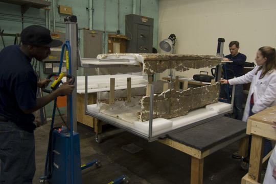 Three staff members using a lift to realign parts of a plaster cast