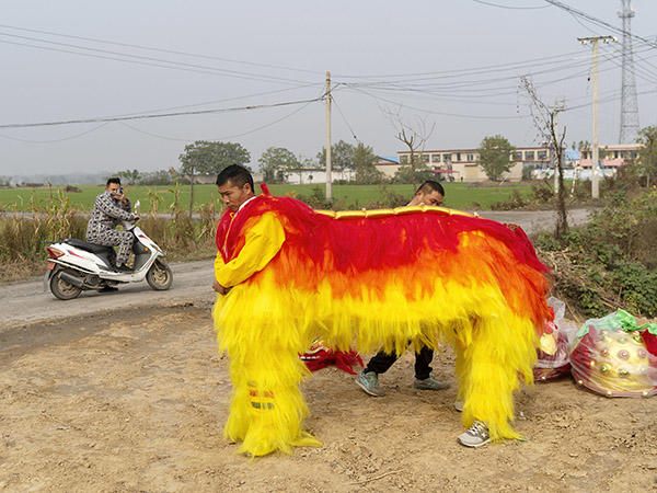 man on motorcycle passes villagers with twin lion festival prop.