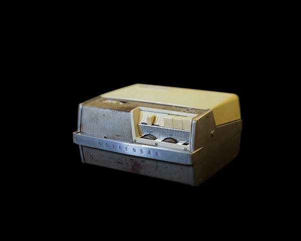 A tape recorder sits against a black background, its edges blur into the black. 
