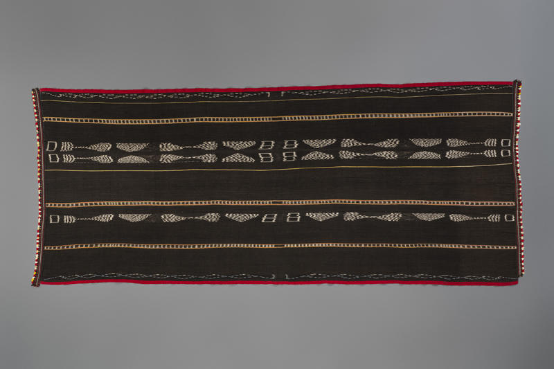 dark blanket with patterns and thin stripes in yellow and white with red and red/white border.