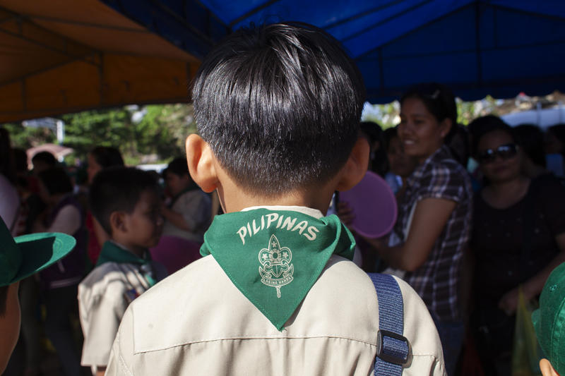 crowd with boy in center facing away from camera wearing pilipinos scout scarf.