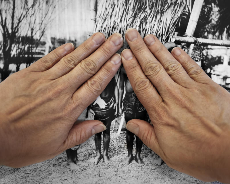 author's hands face down cover majority of historic photo of filipinos on display at 1904 worlds fair.
