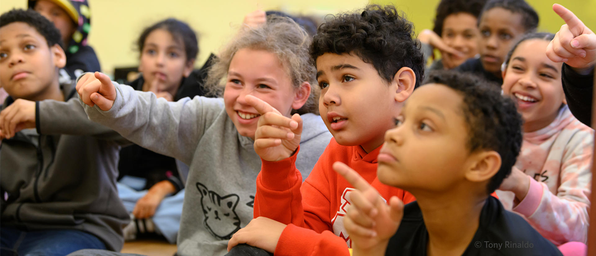 smiling and pointing class of seated students.