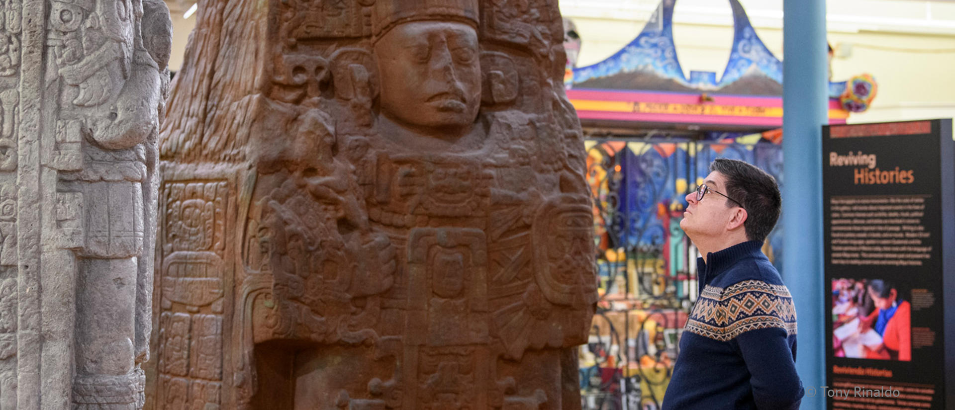 man looks up at large maya sculpture.