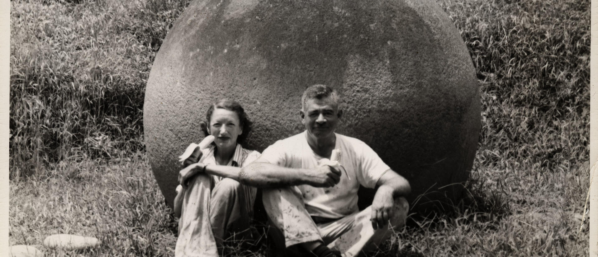 Eleanor Lothrop and Samuel Kirkland Lothrop sitting against stone sphere eating bananas