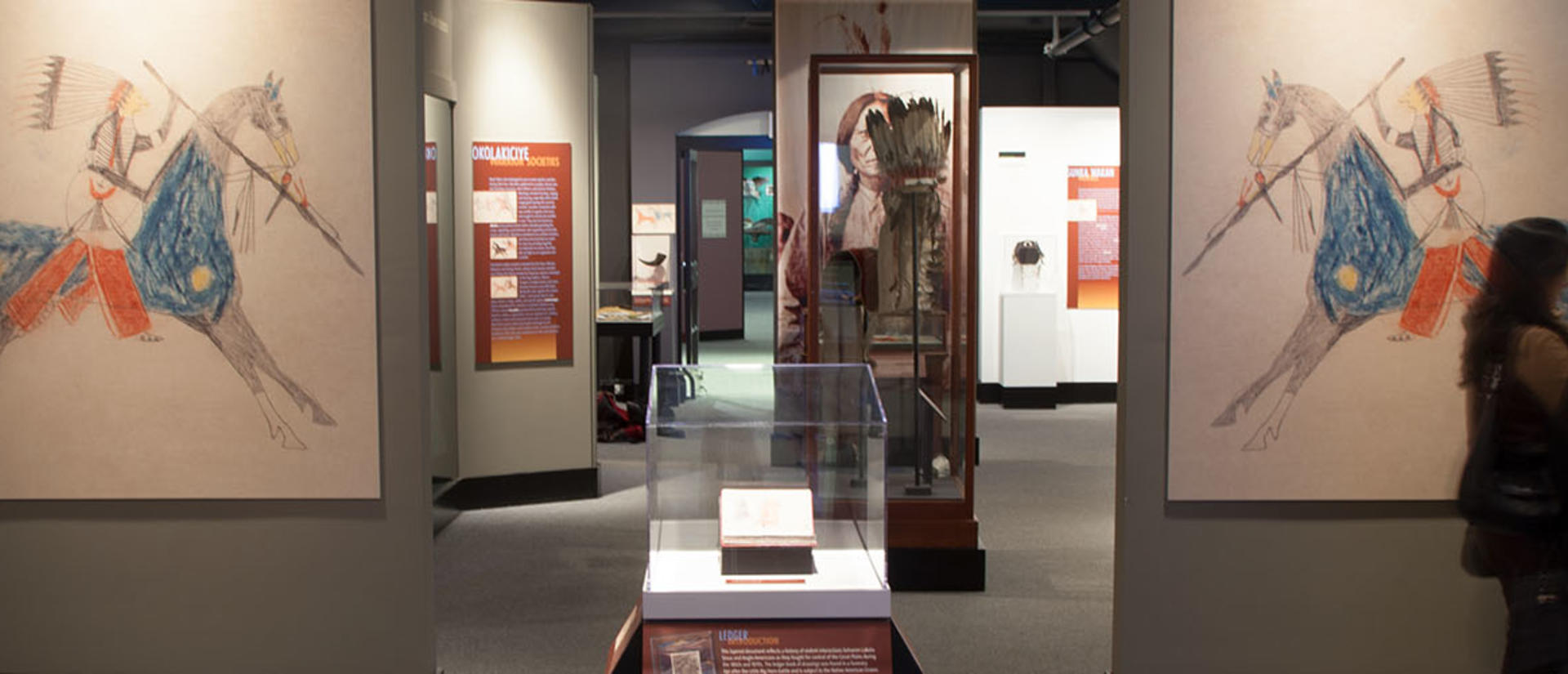 visitors in wide Wiyohpiyata gallery with large color native american drawings.