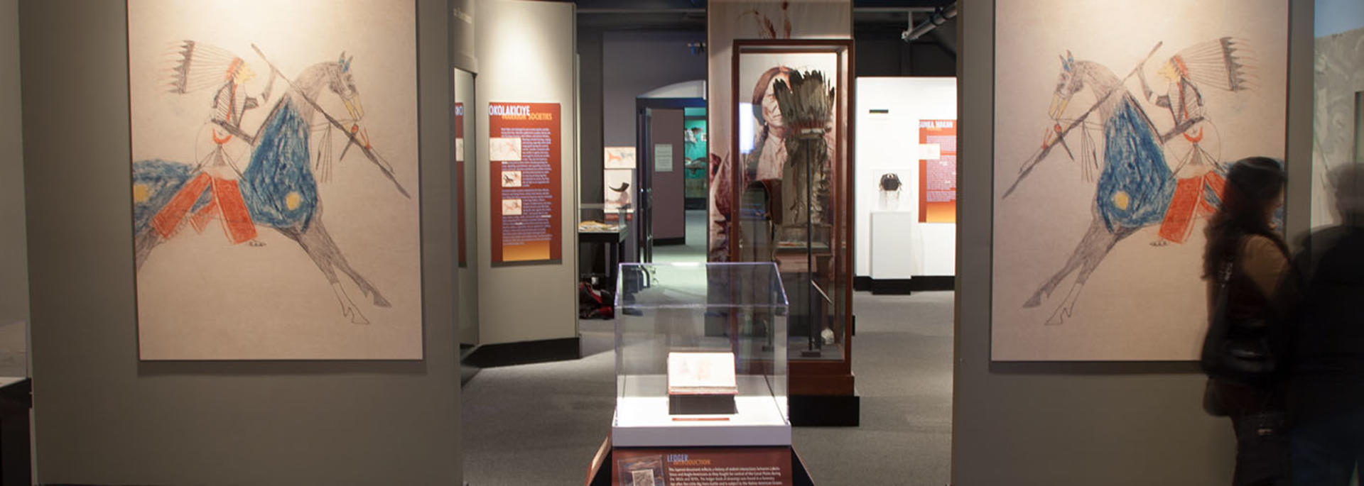 visitors in wide Wiyohpiyata gallery with large color native american drawings.