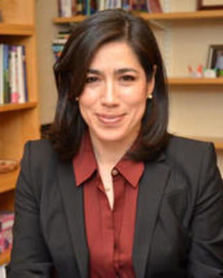 María Luisa Parra-Velasco sits at a desk smiling at the camera, holding a book open in front of her.