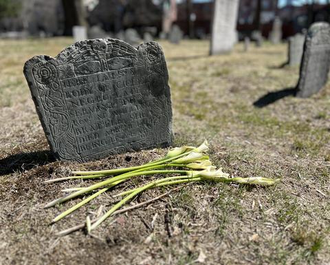 An old headstone in a graveyard with fresh flowers laid before it.
