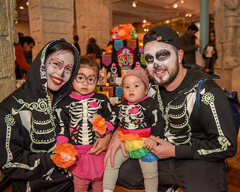 family in skull makeup and skeleton outfits smiling in gallery.